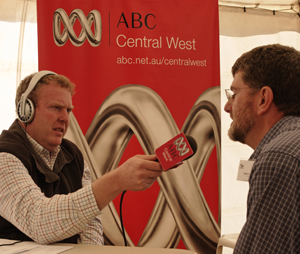 ABC radio journalist Bruce Reynolds (left) points a microphone towards CSIRO ATNF Deputy Director Dr Lewis Ball (right). There is an ABC Central West banner in the background.
