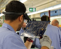 Shot taken from rear right-hand side of male examining an electronics board. Credit: CSIRO.