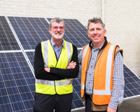 Two men standing in front of solar panels smiling.