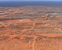 An aerial view of a red desert landscape (the Murchison Radio-astronomy Observatory), with scattered white dish-like antennas joined by connecting dirt roads.