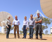 Five people standing in front of large dish-like antennas.