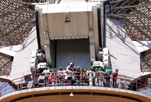 A group of people with green hard hats walk around the azimuth track of the Parkes telescope below the counterweight