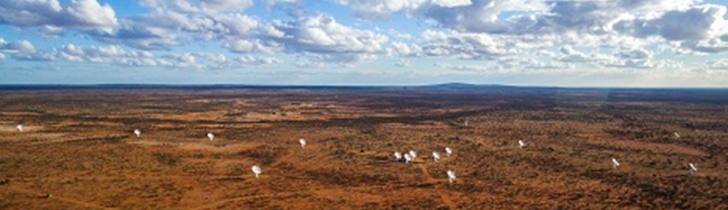 A flat red expanse of country, dotted with ASKAP antenna, with a blue sky above, graced with clouds